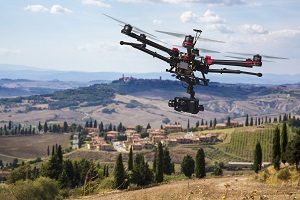 A flying helicopter with raised landing gears and a camera with blured hills of Tuscany in the background